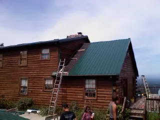 Green metal roof going on a two story log home with ladders set in Caldwell